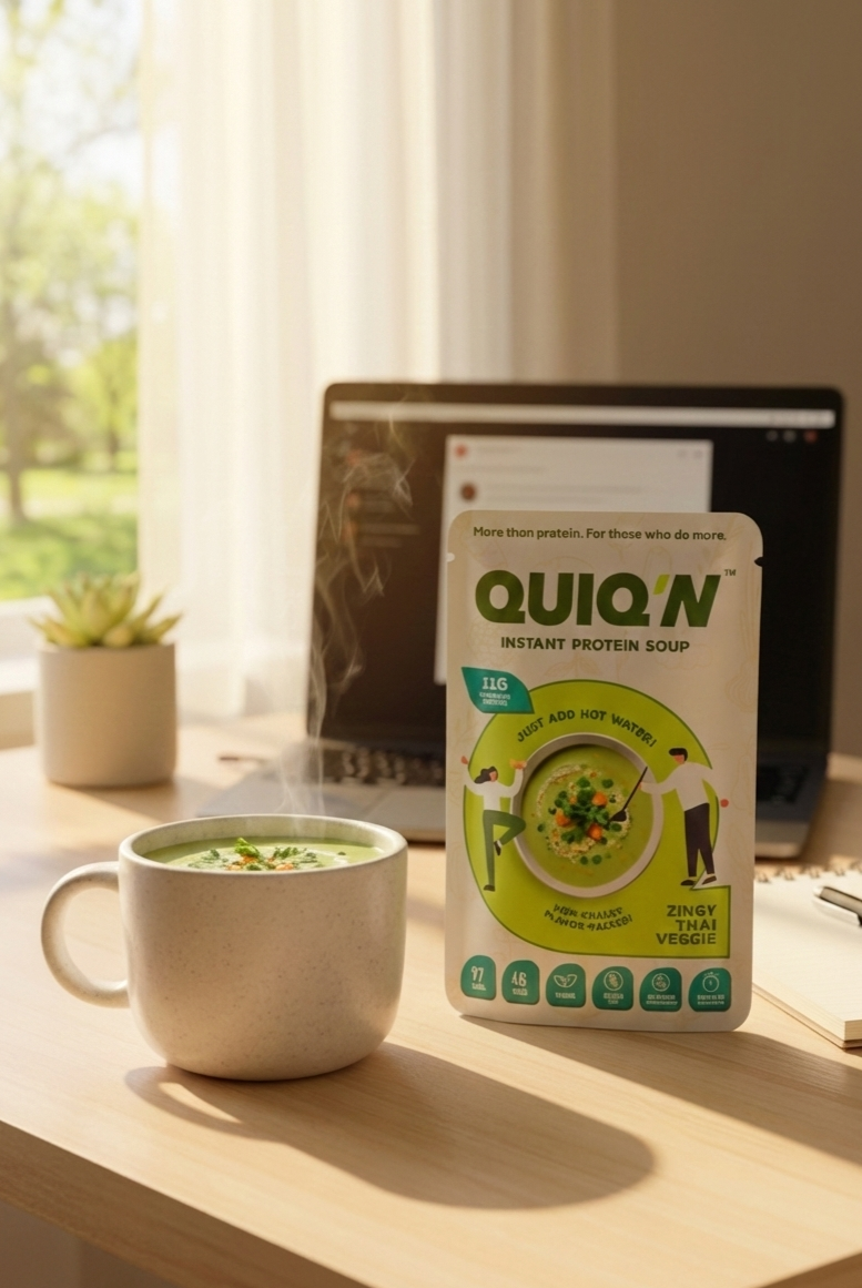 Quiq'N instant protein soup package on a desk with a mug of soup and laptop in the background